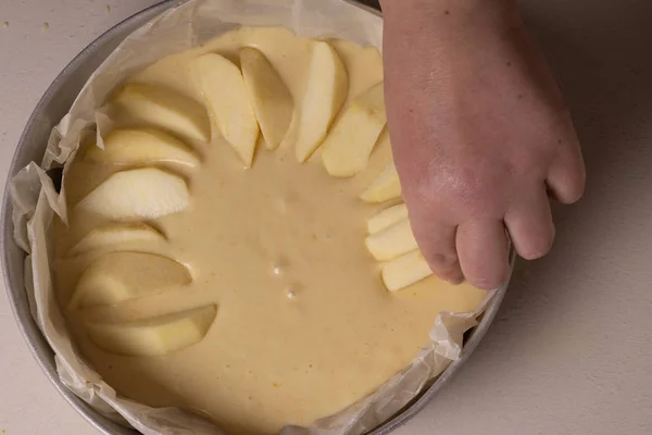 Kvinnliga händer lägger äppelskivor på en kaka innan bakning. — Stockfoto