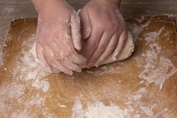 A woman kneads the dough. Plywood cutting board, wooden flour sieve and wooden rolling pin - tools for making dough