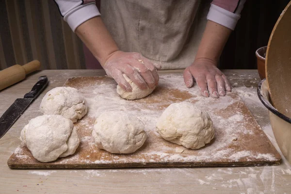 A woman kneads the dough. Plywood cutting board, wooden flour sieve and wooden rolling pin - tools for making dough