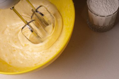 Bir kadın sarı bir kasede turtanın malzemelerini elektrikli mikserle karıştırıyor.