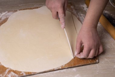 Bir kadın hamuru beyaz seramik bir bıçakla kare kare keser. Çizgi film kesme tahtası, ahşap elek ve ahşap raptiye - hamur yapmak için araçlar