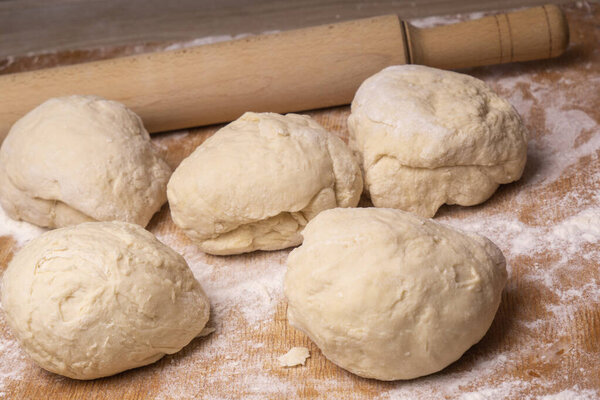 Balls of dough. Plywood cutting board, wooden flour sieve and wooden rolling pin - tools for making dough