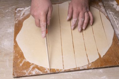 Bir kadın hamuru beyaz seramik bir bıçakla kare kare keser. Çizgi film kesme tahtası, ahşap elek ve ahşap raptiye - hamur yapmak için araçlar