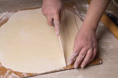 Bir kadın hamuru beyaz seramik bir bıçakla kare kare keser. Çizgi film kesme tahtası, ahşap elek ve ahşap raptiye - hamur yapmak için araçlar