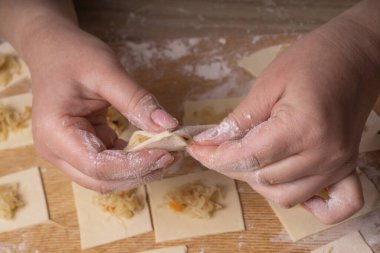 Bir kadın hamur ve lahana karelerinden mantı ve ravioli heykeli yapıyor. Çizgi film kesme tahtası, ahşap elek ve ahşap raptiye - hamur yapmak için araçlar