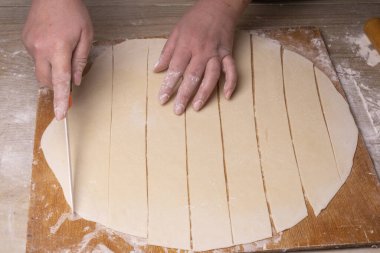 Bir kadın hamuru beyaz seramik bir bıçakla kare kare keser. Çizgi film kesme tahtası, ahşap elek ve ahşap raptiye - hamur yapmak için araçlar