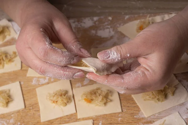 A woman sculpts dumplings and ravioli from squares of dough and cabbage. Plywood cutting board, wooden flour sieve and wooden rolling pin - tools for making dough