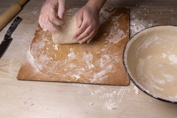 Seorang wanita berlutut adonan. Plywood memotong papan, tepung kayu saringan dan kayu rolling pin alat-alat untuk membuat adonan . — Stok Foto