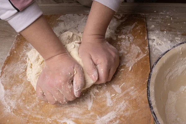 A woman kneads the dough. Plywood cutting board, wooden flour sieve and wooden rolling pin - tools for making dough. — Stock Photo, Image