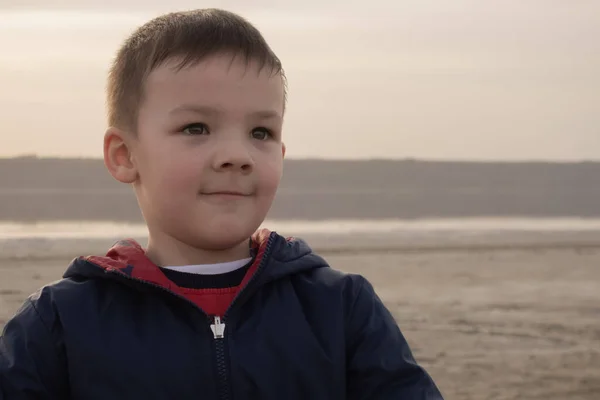 En pojke på 4 år i blå jacka på en tom strand. Barnet ler.. — Stockfoto