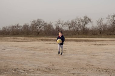 4 yaşındaki bir çocuk boş bir plajda futbol oynuyor.