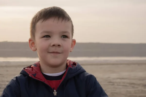 Ένα αγόρι 4 ετών με μπλε μπουφάν σε μια άδεια παραλία. Το μωρό χαμογελάει.. — Φωτογραφία Αρχείου