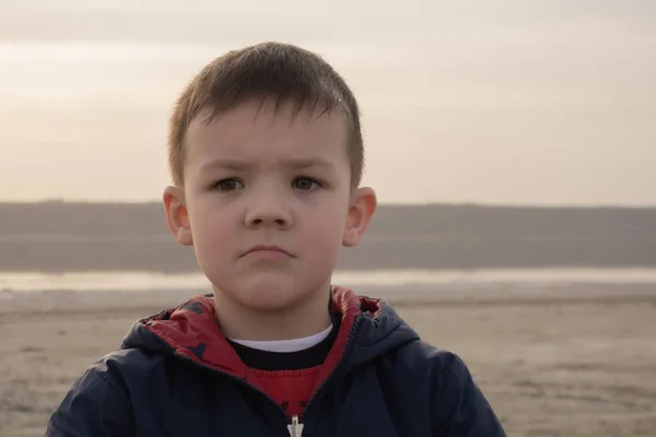 Ένα αγόρι 4 ετών με μπλε μπουφάν σε μια άδεια παραλία. Το παιδί είναι λυπημένο.. — Φωτογραφία Αρχείου