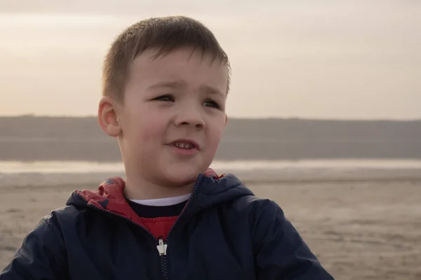 Ένα αγόρι 4 ετών με μπλε μπουφάν σε μια άδεια παραλία. Το μωρό χαμογελάει.. — Φωτογραφία Αρχείου