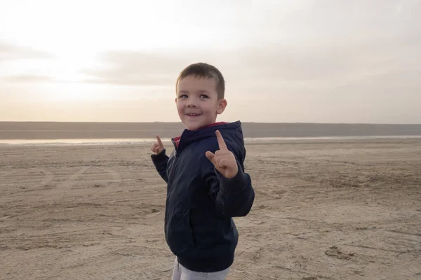 Um rapaz de 4 anos de casaco azul numa praia vazia. Representa um super-herói . — Fotografia de Stock