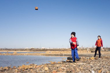 5 ve 10 yaşındaki iki kardeş gölde eğlenip suya taş atıyorlar.