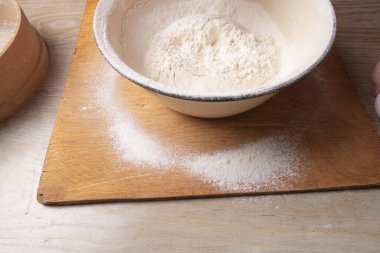 Büyük kâse, kesme tahtası, masada un elemek için elek. Ev mutfağında un toplayan kadın elleri.