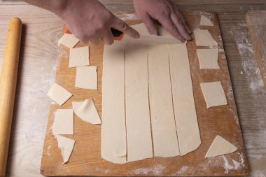 Kadın eli kesme tahtasındaki hamuru beyaz bir bıçakla keser. Evde yemek pişirmek.