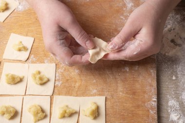 Kadın elleri, hamurdan yapılmış hamur köftelerini patatesle yontuyor. Evde yemek pişirmek.