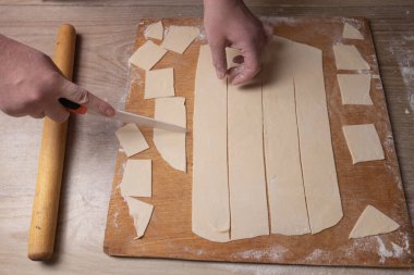 Kadın eli kesme tahtasındaki hamuru beyaz bir bıçakla keser. Evde yemek pişirmek.