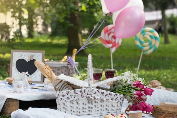 Picnic decorations, cannotier, flowers, fruits. Picnic at the park on the grass: tablecloth, basket, healthy food and accessories, top view, bread, baguette, alcohol, big lollipops. Happy mothers day. — Stock Photo, Image