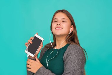 Modadan anlayan tatlı bir kız kulaklıkla müzik dinliyor, mavi arka planda pembe bir elbise giyiyor.