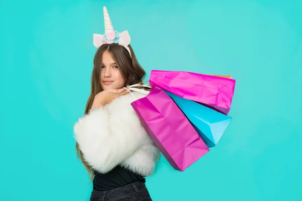 Portrait of a smiling pretty girl with shopping bags over blue background. Black friday concept. Kawaii teenage girl. Cute young woman with unicorn horn. — ストック写真