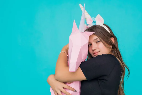 Kawaiská puberťačka. Roztomilá mladá žena s jednorožec rohu držení a objímání ručně vyrobený papír růžový jednorožec přes modré pozadí. — Stock fotografie