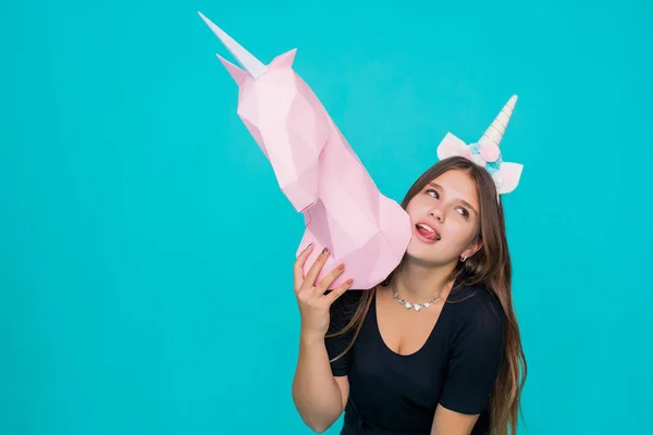 Adolescente Kawaii. Linda mujer joven con cuerno de unicornio sosteniendo papel hecho a mano unicornio rosa sobre fondo azul . —  Fotos de Stock