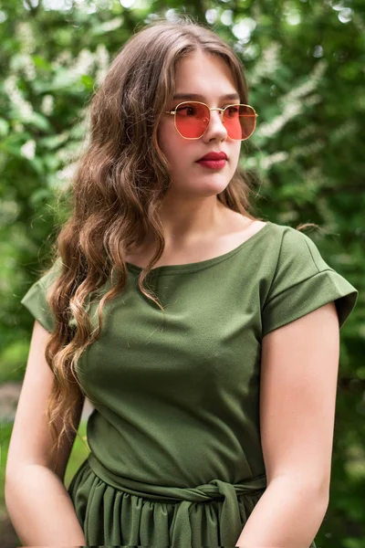 Porträt eines jungen Mädchens mit grünem Kleid und roter Sonnenbrille. Nahaufnahme. Plus-Größe-Modell. — Stockfoto