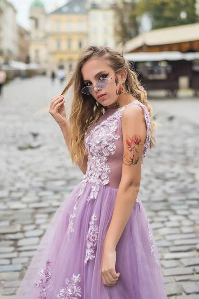 Portrait of young gil wearing dress and violet sunglasses. tattoes over her arms and face. Close up. City walk. Subculture attributes. — Stockfoto