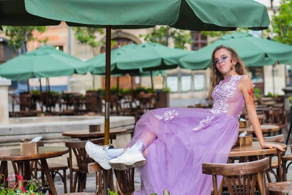 Retrato do jovem gil vestindo vestido e óculos de sol violeta sentado na mesa de cafés. tatuagens nos braços e na cara. Fecha. Caminhada. Atributos da subcultura . — Fotografia de Stock