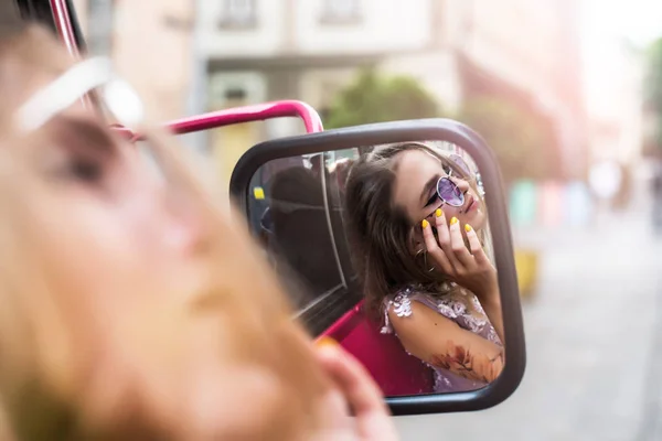 Retrato de gil joven con vestido y gafas de sol violeta. tatuajes sobre sus brazos y la cara mirando en el espejo del coche. De cerca. Paseo por la ciudad. Atributos de subcultura . —  Fotos de Stock