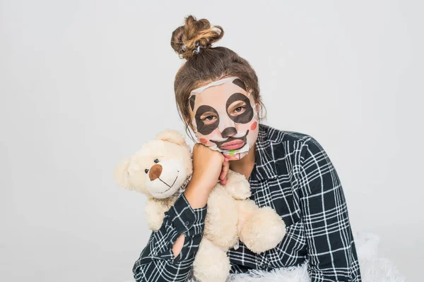 Joven adolescente con máscara de panda facial mirando a la cámara sobre fondo blanco. Procedimiento cosmético. Spa de belleza y cosmetología . —  Fotos de Stock