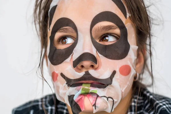 Joven adolescente con máscara de panda facial mirando a la cámara sobre fondo blanco. Procedimiento cosmético. Spa de belleza y cosmetología . — Foto de Stock