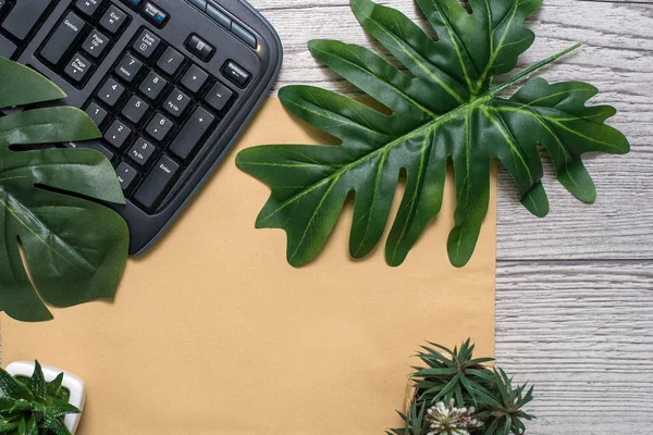 Flat lay, top view office table desk. Workspace with blank clip board, keyboard, office supplies, pot, monstera leaf on wooden background. office products and stationery framed.