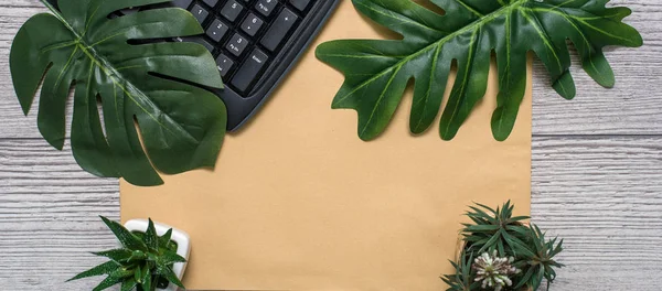 Flat lay, top view office table desk. Workspace with blank clip board, keyboard, office supplies, pot, monstera leaf on wooden background. office products and stationery framed.