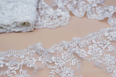 Doku danteli kumaş. Beyaz arka plan stüdyosunda dantel. İplik ya da iplikten yapılmış ince kumaş. Fildişi renkli dantel kumaşın arkaplan resmi. Bej arkaplanda beyaz dantel.