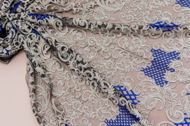 Doku danteli kumaş. Beyaz arka plan stüdyosunda dantel. İplik ya da iplikten yapılmış ince kumaş. Fildişi renkli dantel kumaşın arkaplan resmi. Bej arka planda gümüş ya da altın ve mavi dantel.