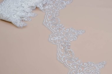 Doku danteli kumaş. Beyaz arka plan stüdyosunda dantel. İplik ya da iplikten yapılmış ince kumaş. Fildişi renkli dantel kumaşın arkaplan resmi. Bej arkaplanda beyaz dantel.
