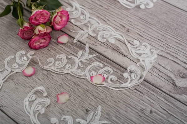 Bílé dřevěné pozadí s bílými jarními květy růží a krajkové stuhy. Šťastný den žen. Textura krajky na dřevěném pozadí. — Stock fotografie