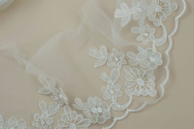 Doku danteli kumaş. Beyaz arka plan stüdyosunda dantel. İplik ya da iplikten yapılmış ince kumaş. Fildişi renkli dantel kumaşın arkaplan resmi. Bej arkaplanda beyaz dantel.