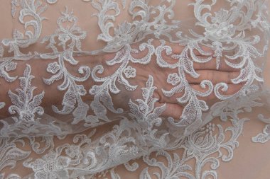 Doku danteli kumaş. Beyaz arka plan stüdyosunda dantel. İplik ya da iplikten yapılmış ince kumaş. Fildişi renkli dantel kumaşın arkaplan resmi. Bej arkaplanda beyaz dantel.