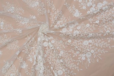 Doku danteli kumaş. Beyaz arka plan stüdyosunda dantel. İplik ya da iplikten yapılmış ince kumaş. Fildişi renkli dantel kumaşın arkaplan resmi. Bej arkaplanda beyaz dantel.