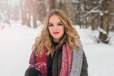 Noel, yeni yıl, kış tatili konsepti. Kıvırcık saçlı tatlı bir genç kız. Parkta karla oynamak.