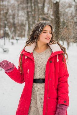 Noel, yeni yıl, kış tatili konsepti. Kıvırcık saçlı tatlı bir genç kız. Parkta karla oynamak.