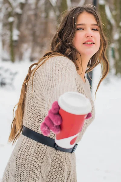 Belle adolescente mignonne et souriante avec maquillage naturel et cheveux bouclés légers tient une tasse avec du café chaud ou du thé. Saison d'hiver. Noël, Nouvel An, concept vacances d'hiver . — Photo