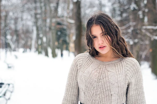 Kültéri közeli portré fiatal gyönyörű tizenéves lány hosszú haj visel pulóver pózol az erdőben. Karácsony, téli ünnepek. Havazik. Másolás, üres hely a szövegnek — Stock Fotó