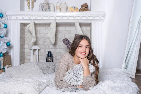 Feliz adolescente sentada cerca del árbol de Navidad. Jovencita feliz con regalos de pelo rizado junto a la chimenea cerca del árbol de Navidad. Concepto de año nuevo. Navidad.. —  Fotos de Stock