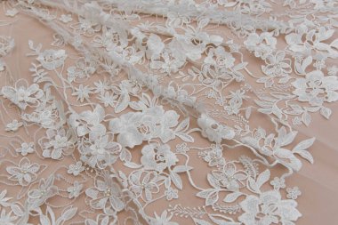 Doku danteli kumaş. Beyaz arka plan stüdyosunda dantel. İplik ya da iplikten yapılmış ince kumaş. Fildişi renkli dantel kumaşın arkaplan resmi. Bej arkaplanda beyaz dantel.